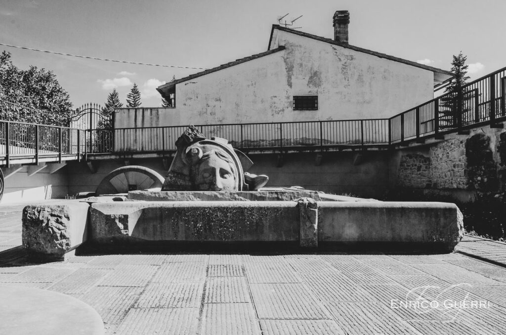Fontana in pietra fotografata in bianco e nero in una piazza