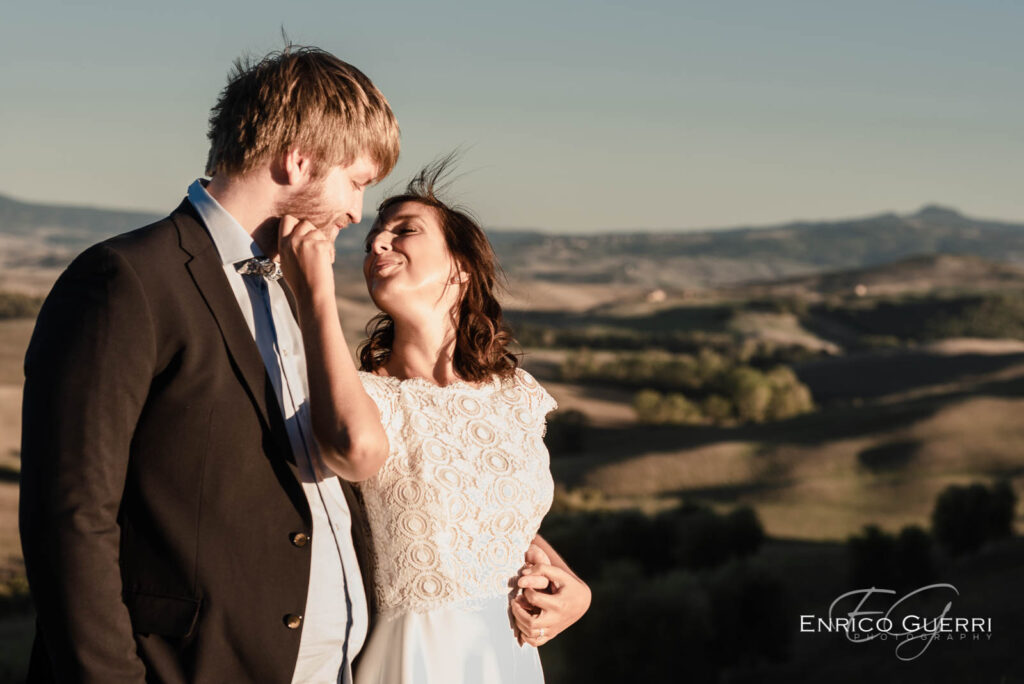 Sposa sorride accarezzando lo sposo nella campagna della Val d’Orcia