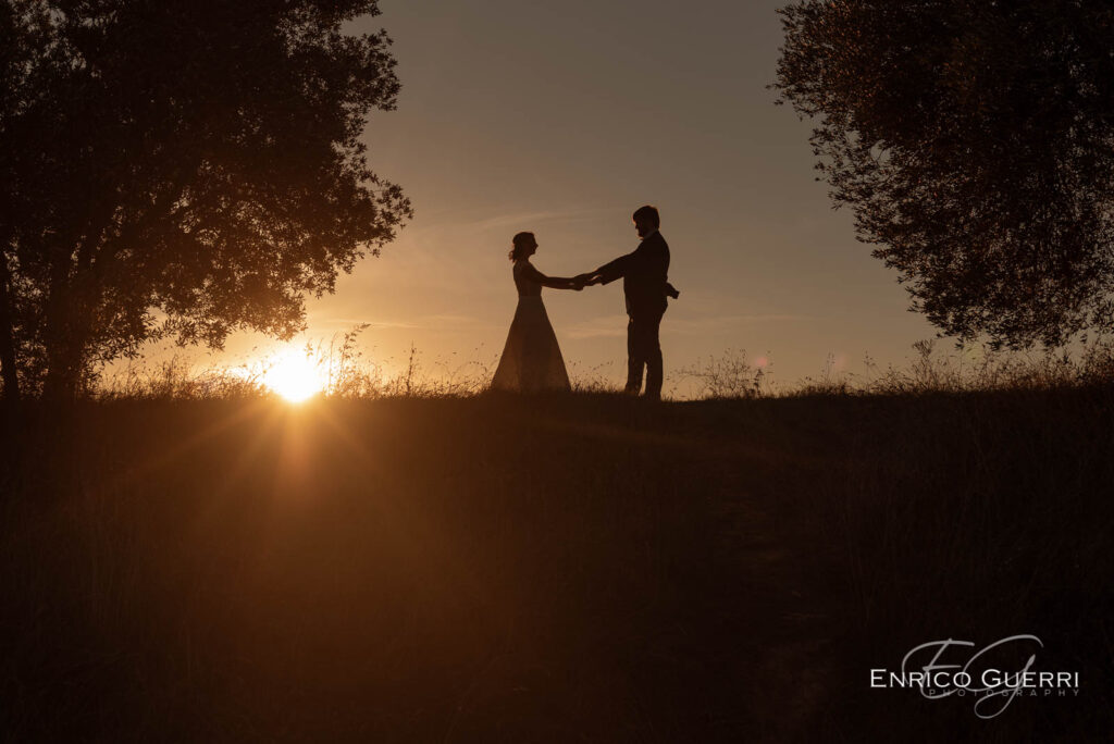 Sposi si tengono per mano in silhouette davanti al sole al tramonto